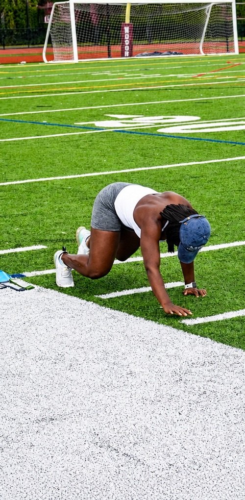 Shevane doing bear crawls across a turf field during outdoor training